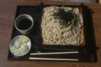 "zaru soba" cold buckwheat  noodles with "tsuyu" soy sauce-based dipping soup  small plate contains chopped "negi"  Japanese leeks  and wasabe paste