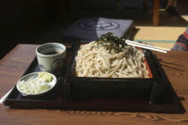 "zaru soba" cold buckwheat noodles with chilled "tsuyu"   soy sauce-based dipping soup  and small plate contains chopped "negi"  Japanese leek  and wasabe