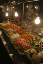 Namdaemun Market on a cold December night with a woman cooking behind trays of fresh seafood  pork  chicken and beef with plastic sheeting to keep out cold