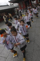 Asakusa. 4 year old nursery students from Senso-ji Dembo-in Nursery  carrying flowers to present to Buddha as part of his birthday celebrations  accopamied by Buddhist monk
