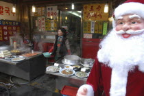 Namdaemun Market in December. Streetside restaurant with Santa Claus outside and a woman cook in the background