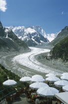 Chamonix.  People sitting at outside tables of terrace restaurant looking out across glacier and the Alps beyond.