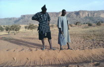 A Diviner and Dogon client explains marks left in sand by desert fox over the marks he made the day before.