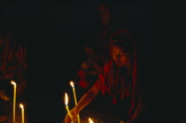 Woman making prayers with candles in red light.  Disappearing World