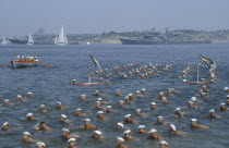 Navy Day. Sailors swimming in the sea in formation with battleships behind.Mutual goal in accord individuals working towards the same goal.