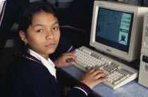 School girl learning computer sitting in class looking towards camera.