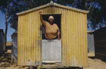 Woman standing with her fist in air looking out of a yellow corrugated hut a resident of Malmsbury council Hostel.