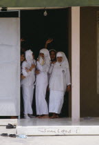 Muslim college girls dressed in white standing at a door entrance.Moslem