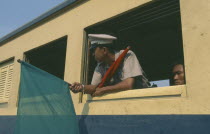 Guard on train to Ayutthaya leaning out of carriage window with red and green flags.