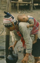 Akha tribeswoman carrying baby on her back while collecting well water.I-Kaw