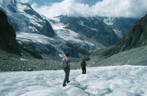 Hikers walking down glacier wearing sun glasses and carrying umbrella to protect against sun.