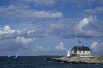 Headland with small building and lighthouse and passing sailboats