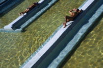 Man and woman lying on raised tiled area above water level in spa.