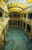 Gellert Baths.  Interior with bathers in swimming pool lined with carved pillars and with domed glass roof above.