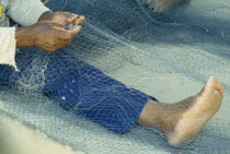 Fishermen repairing nets on the beach  view of bare feet  hands and nets.
