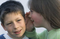 Young girl whispering into the ear of a boy.