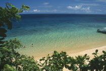 Panuba Bay  north west coast.  Sandy beach and aquamarine sea with tourist couple bathing.  View partly framed by tree branches.