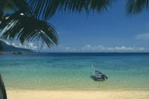 Panuba Bay  north west coast.  Empty  sandy beach and blue painted boat in shallow water at its edge.  View over sea towards horizon partly framed by palm tree branches.