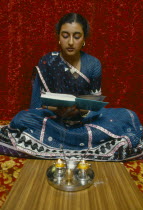 England.  Girl reading Holy book in front of lighted candles and incense during Dirwali.