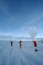 Three figures launching a balloon to measure amounts of ozone in the air at various altitudes.  US Amundsen-Scott South Pole Station.