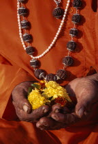 Close up of hands holding flowers for votive offering including prayer beads