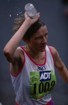 Competitor in London Marathon pouring bottle of water over her head to keep cool.