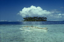 Outrigger boat in clear sparkling water and Motu with large white cloud above. French PolynesiaIsletFrench PolynesiaIslet