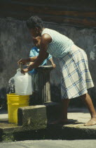 Woman and young boy collecting water from outside stand pipe
