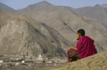 Tibetan Monk sitting on hillside overlooking Xiahe Monastery