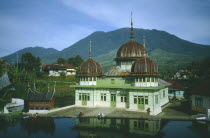 Mosque with rusty tin domes by a lake with people sitting at the waters edge
