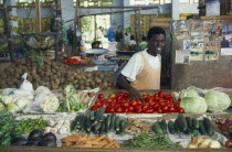 Smiling vendor behind fruit and vegetable stall in Zanzibar town.