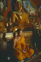 Young monk praying beneath seated golden Buddha figures