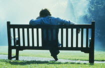 Thoughtful single man sitting on park bench in slumped posture.