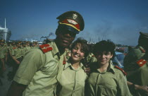 Two girls in soldiers uniforms stand with soldier