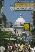 Busy street scene with people  hanging shop signs and dome of white building beyond.