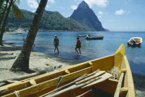 People walking along beach with boats moored offshore and the Pitons beyond and prow of boat in imediate foreground.Windward IslandsWindward Islands