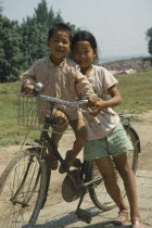 Two children sharing an adult bicycle
