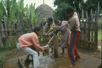 Group of laughing children collecting water at hand pump.