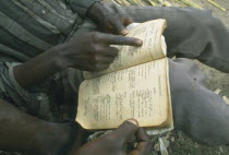 Kaala.  Displaced men living in disused factory practising reading skills with Portuguese grammer book.