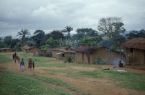 Mud brick village houses with people on unmade road outside.