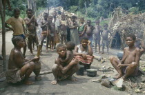 Pygmy group in village clearing surrounded by thatched huts. Zaire