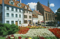 Church of St John beside town housing with colourful flowerbeds in the foreground on Skunu Street. Colorful
