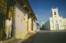 Pastel coloured houses lining Playa de San Juan de Dios and Iglesia San Juan de Dios with man opening metal screen of house doorway in the foreground. Colored
