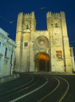 Alfama.  Se Cathedral exterior facade at night with two castellated bell towers and rose window.