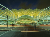 Exterior of bus station on the Expo site illuminated at night with light trails from passing traffic and people in blurred movement in foreground.