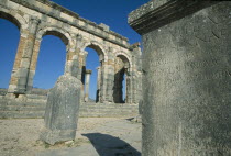 The Basilica.  Cropped view of stone block inscribed with Roman script with arches and colonnade built into wall beyond.