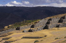 Sacsayhuaman inca site  people walking round the old walls and a cross in the background.