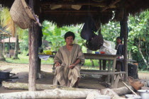 Machiguenga indian man under a shelter and surrounded by traditional domestic items.