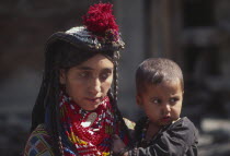 Mother wearing lots of colourful beaded necklaces  holding Kalash boy.