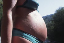 Pregnant woman in a bikini with water droplets on tummy.